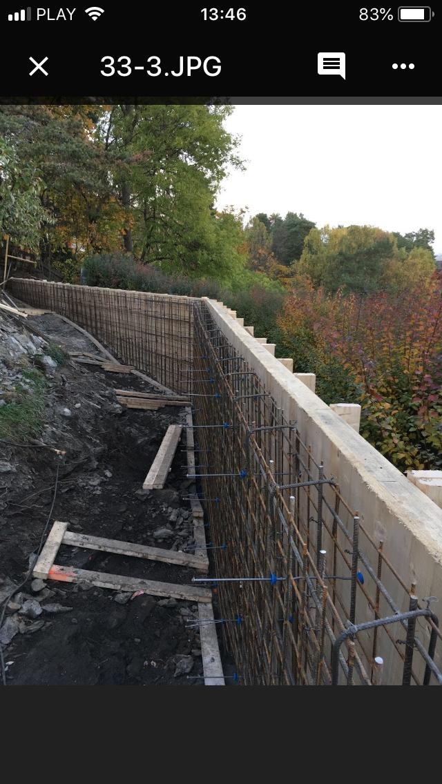 Zbrojenie ściany oporowej z betonu z widocznymi elementami szalunku i otaczającym terenem zielonym w tle.