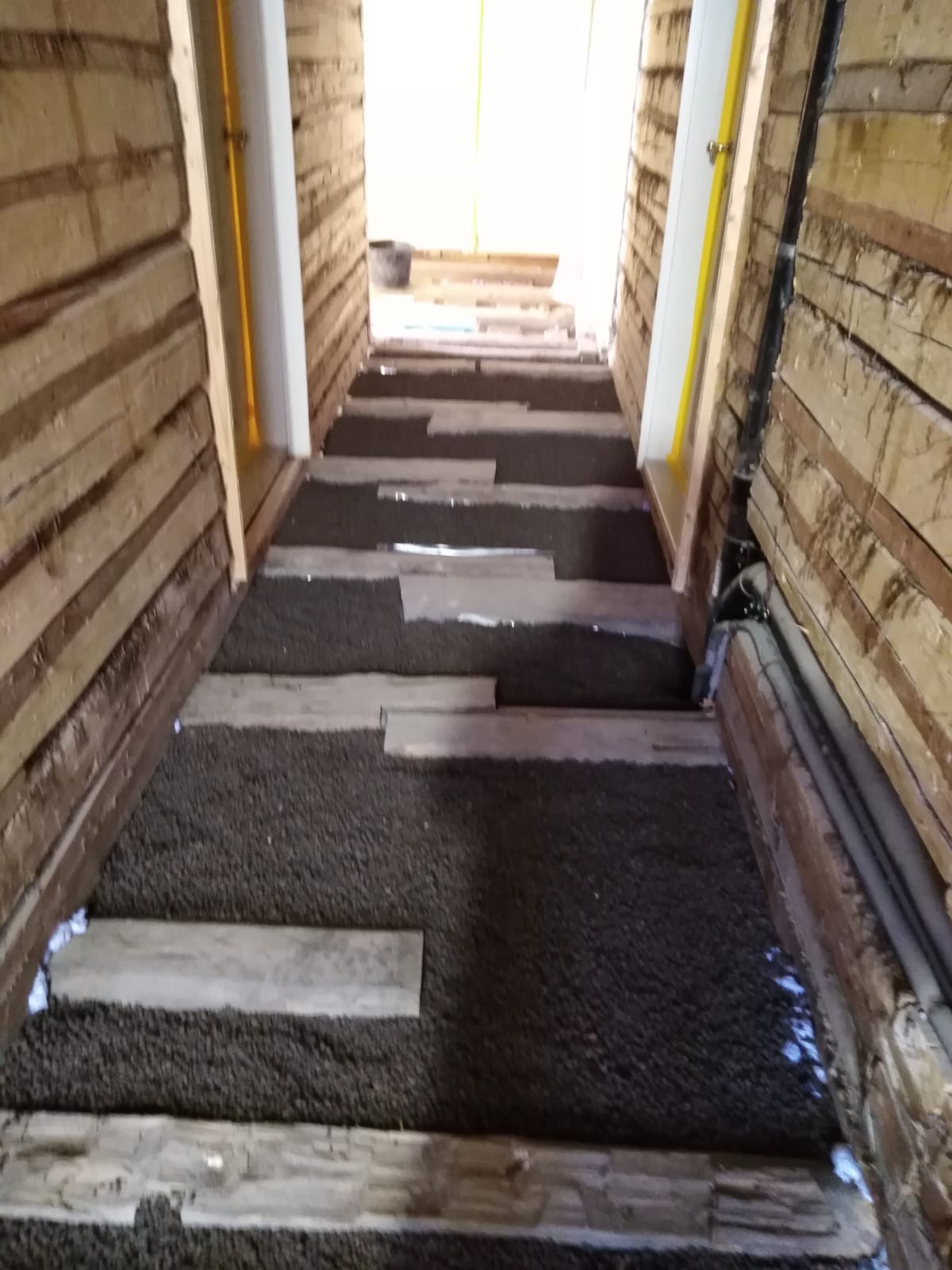 Podłoga w trakcie remontu: widoczne drewniane legary, izolacja z granulatu oraz deski tworzące tymczasowe przejście.