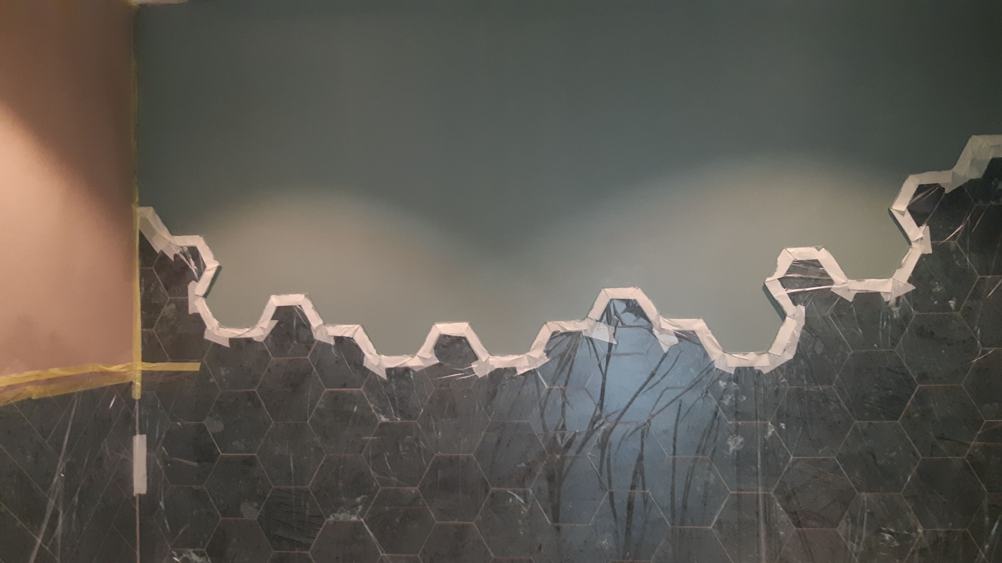 Montaż heksagonalnych płytek na ścianie, zabezpieczonych taśmą malarską, w trakcie prac wykończeniowych.