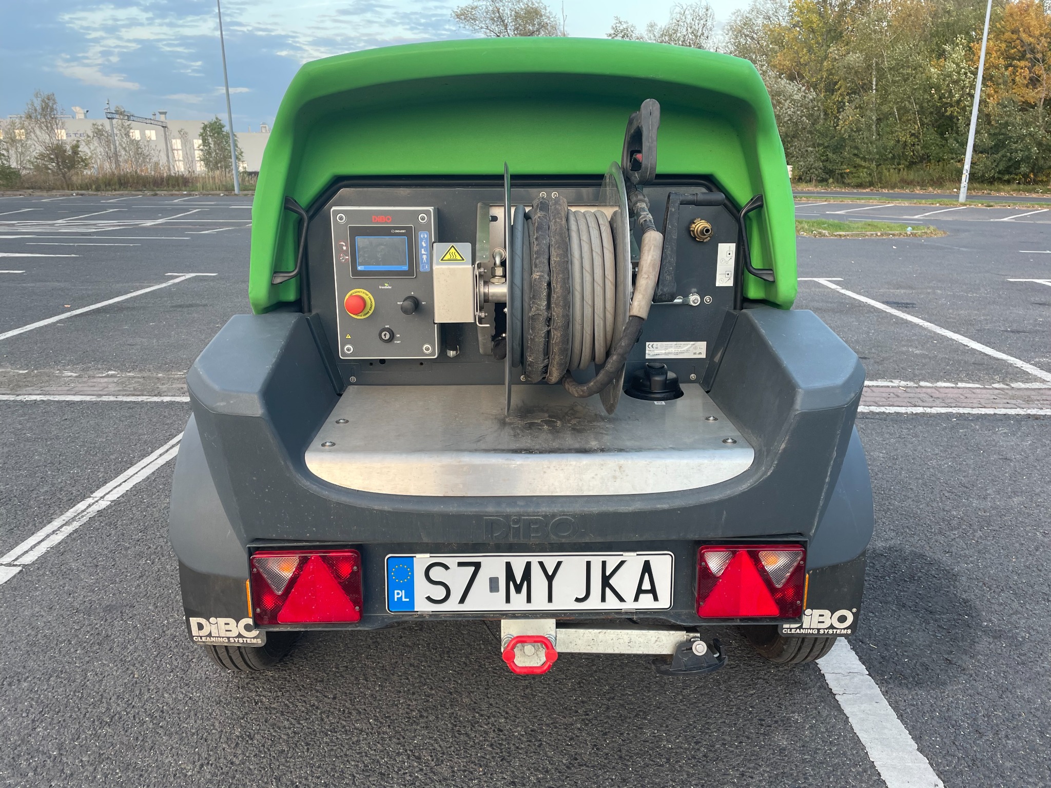 Przenośne urządzenie wysokociśnieniowe DIBO z nawiniętym wężem, panelem sterowania i tablicą rejestracyjną S7 MY JKA, stojące na parkingu.