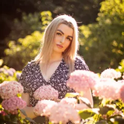 Portret kobiety w kwiecistej sukience, pozującej wśród kwitnących hortensji w Łodzi, z delikatnym oświetleniem słonecznym i rozmytym tłem.