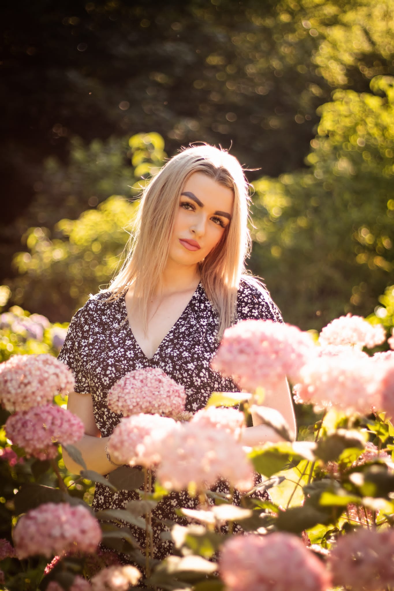 Portret kobiety w kwiecistej sukience, pozującej wśród kwitnących hortensji w Łodzi, z delikatnym oświetleniem słonecznym i rozmytym tłem.