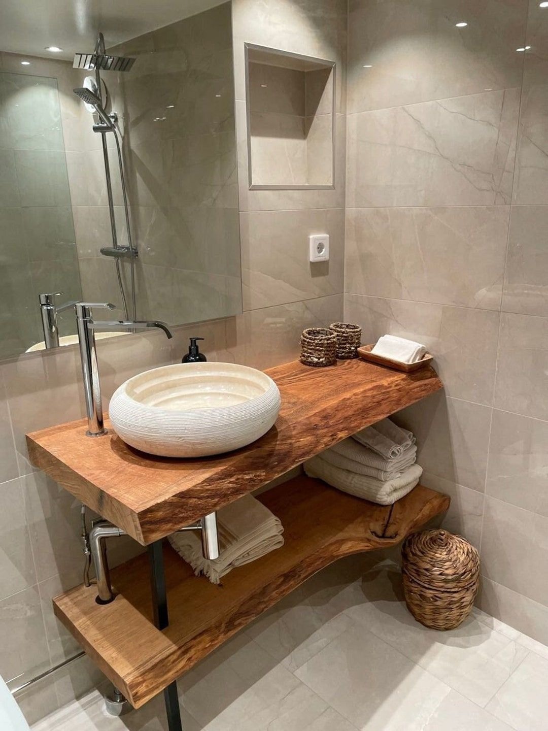 Nowoczesna łazienka z umywalką nablatową w kształcie misy na drewnianym blacie z naturalną krawędzią, metalowa armatura, beżowe płytki i dekoracyjny koszyk z trawy morskiej.