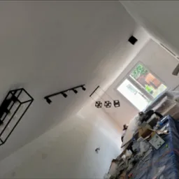 Wnętrze w trakcie remontu z zamontowanym nowoczesnym oświetleniem: czarna, geometryczna lampa sufitowa, reflektory punktowe na szynie oraz lampy wiszące z kloszami w kształcie sześcianów.