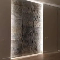 Ściana wyłożona kamieniem dekoracyjnym z podświetleniem LED, widoczna drewniana podłoga i fragment lampy sufitowej.