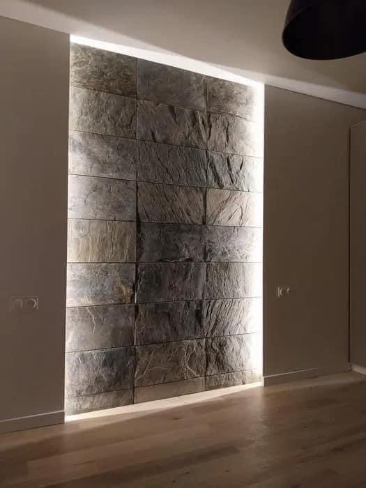 Ściana wyłożona kamieniem dekoracyjnym z podświetleniem LED, widoczna drewniana podłoga i fragment lampy sufitowej.