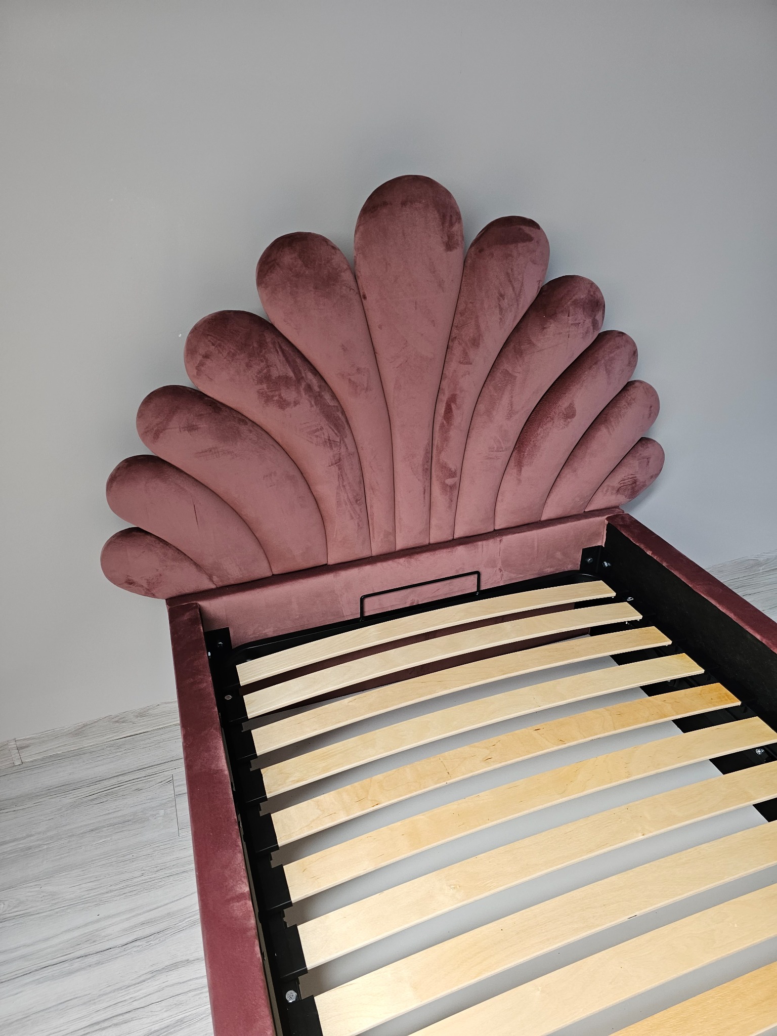 Różowe, welurowe łóżko z zagłówkiem w kształcie muszli, widok z góry na drewniany stelaż, minimalistyczne wnętrze.