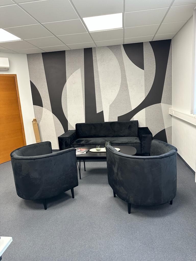 Czarne, welurowe fotele klubowe i sofa w minimalistycznym wnętrzu z geometryczną tapetą w odcieniach szarości, na stoliku kawa i gazety.