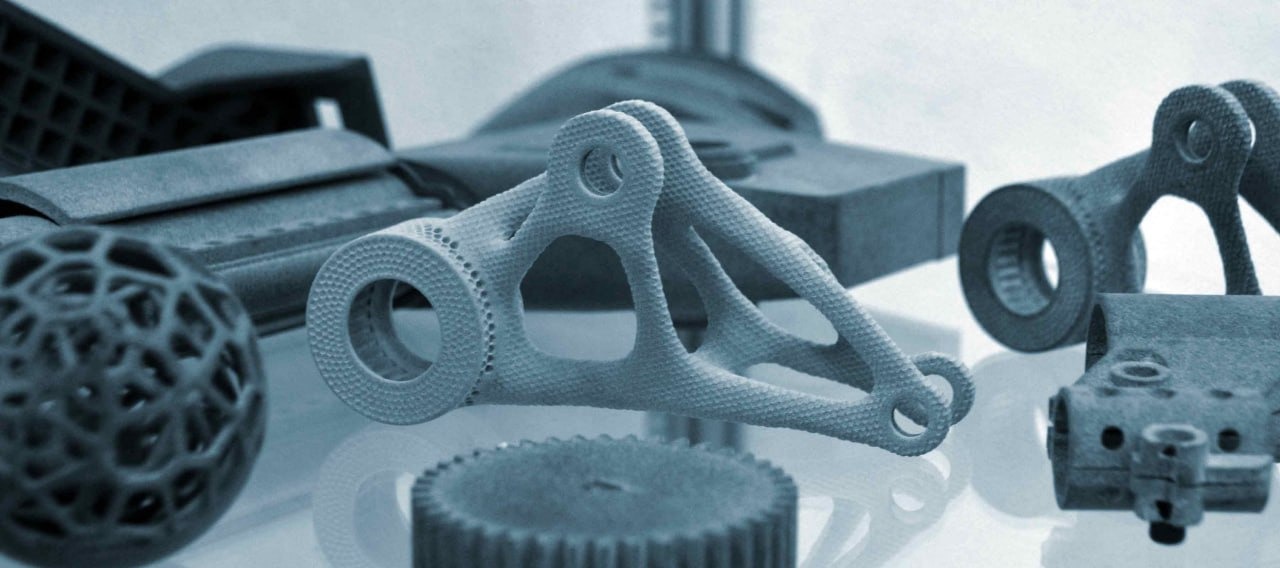 Różne metalowe elementy wykonane z wykorzystaniem technologii CNC, w tym ażurowa kula, koło zębate i element konstrukcyjny z otworami, na błyszczącej powierzchni.