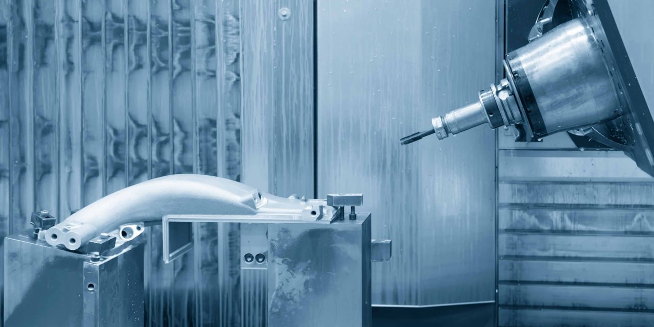 Metalowy element obrabiany wewnątrz maszyny CNC, widoczne narzędzie tnące zbliżające się do detalu zamocowanego na uchwycie.