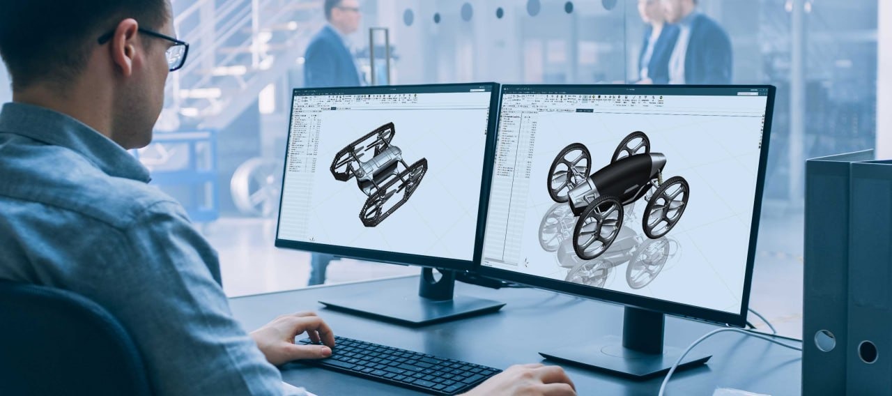 Inżynier projektuje w programie CAD model pojazdu terenowego z napędem gąsienicowym i kołowym na dwóch monitorach.