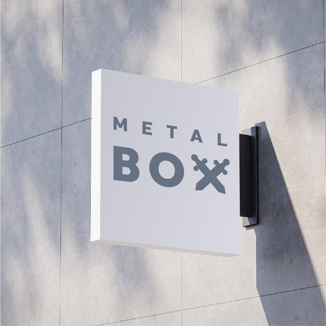Kwadratowy szyld reklamowy z napisem 'METAL BOX' i symbolem skrzyżowanych mieczy, zamocowany na szarej, betonowej ścianie w cieniu drzewa.