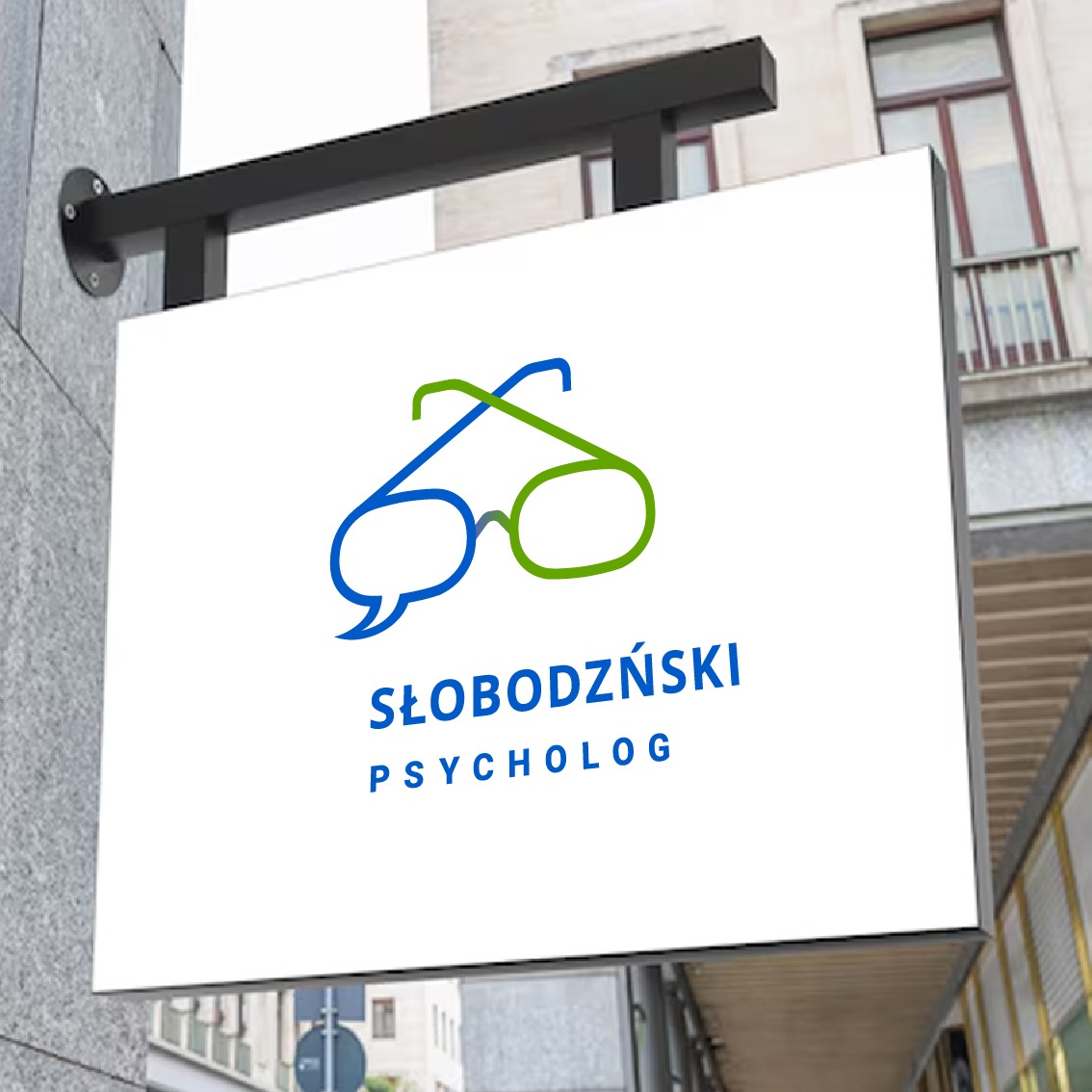 Szyld reklamowy z logo w kształcie okularów i dymku dialogowego, w kolorach niebieskim i zielonym, z nazwą 'SŁOBODZIŃSKI PSYCHOLOG' na tle budynku.