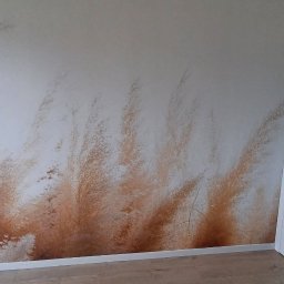 Usługi ogólnobudowlane Dariusz Perlikiewicz - Ściana w pokoju z fototapetą przedstawiającą pampasową trawę, widoczna część okna balkonowego i biała szafa wnękowa.