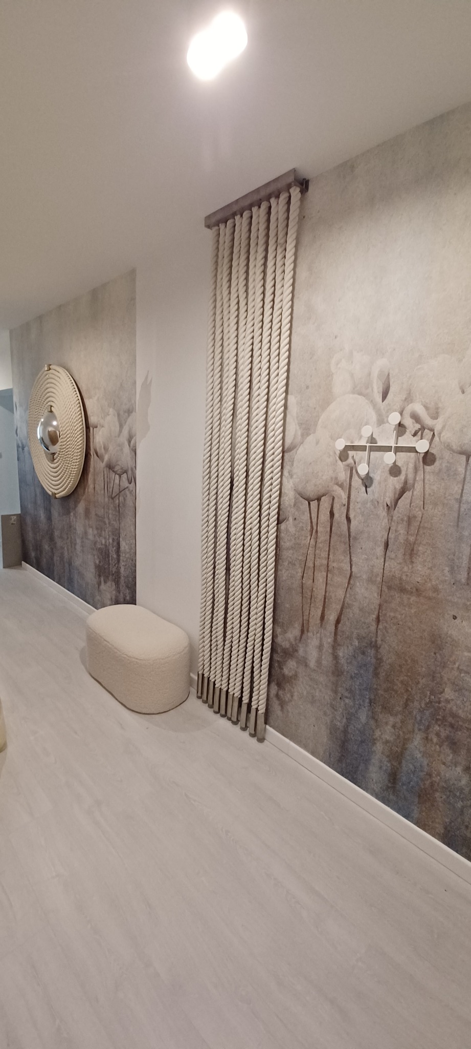 Nowoczesny przedpokój z tapetą w motywy ptaków, dekoracyjnym lustrem z liny, pufą i pionową ozdobą ze sznurów na metalowej konstrukcji.