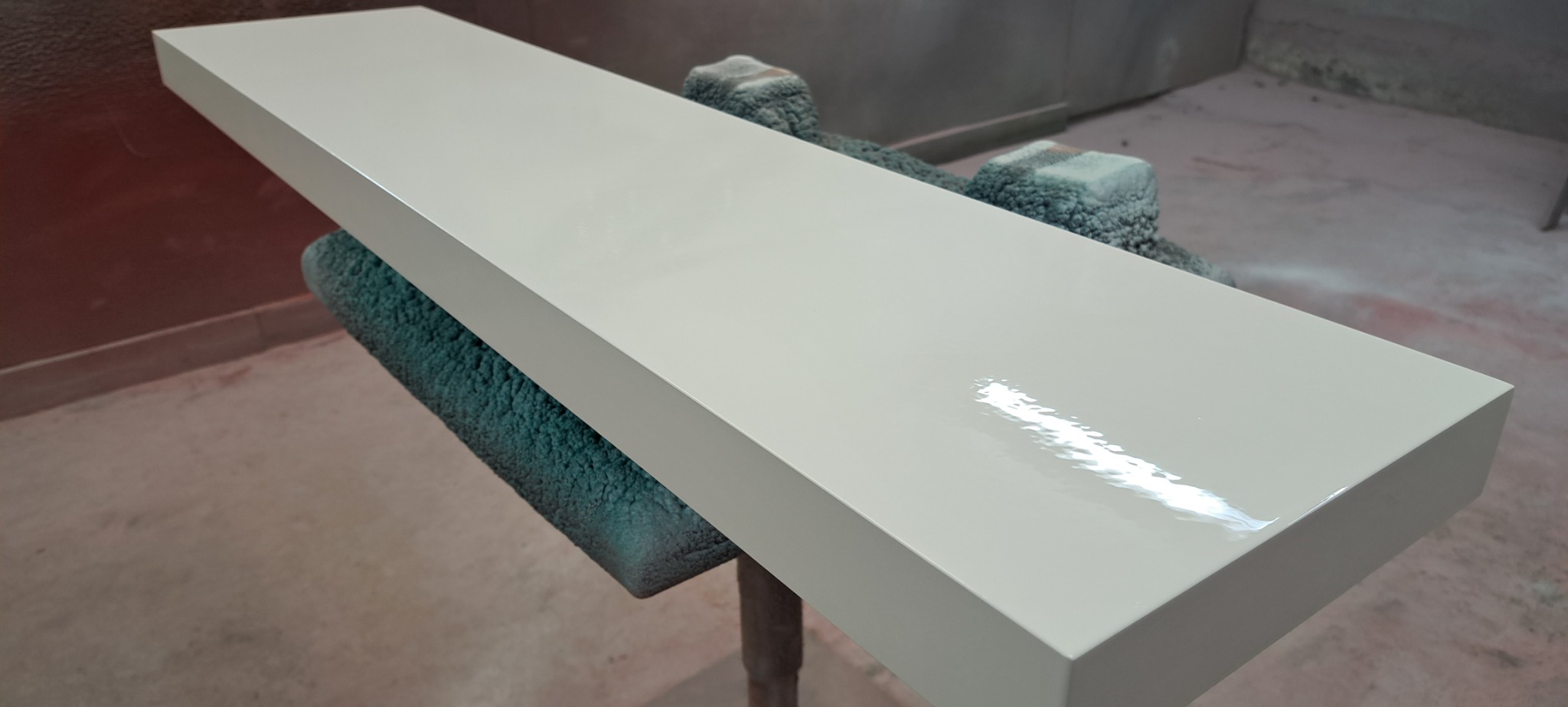 Pomalowany na kremowo blat drewniany, połyskujący jeszcze od świeżej farby, ustawiony na podkładkach w pomieszczeniu warsztatowym.