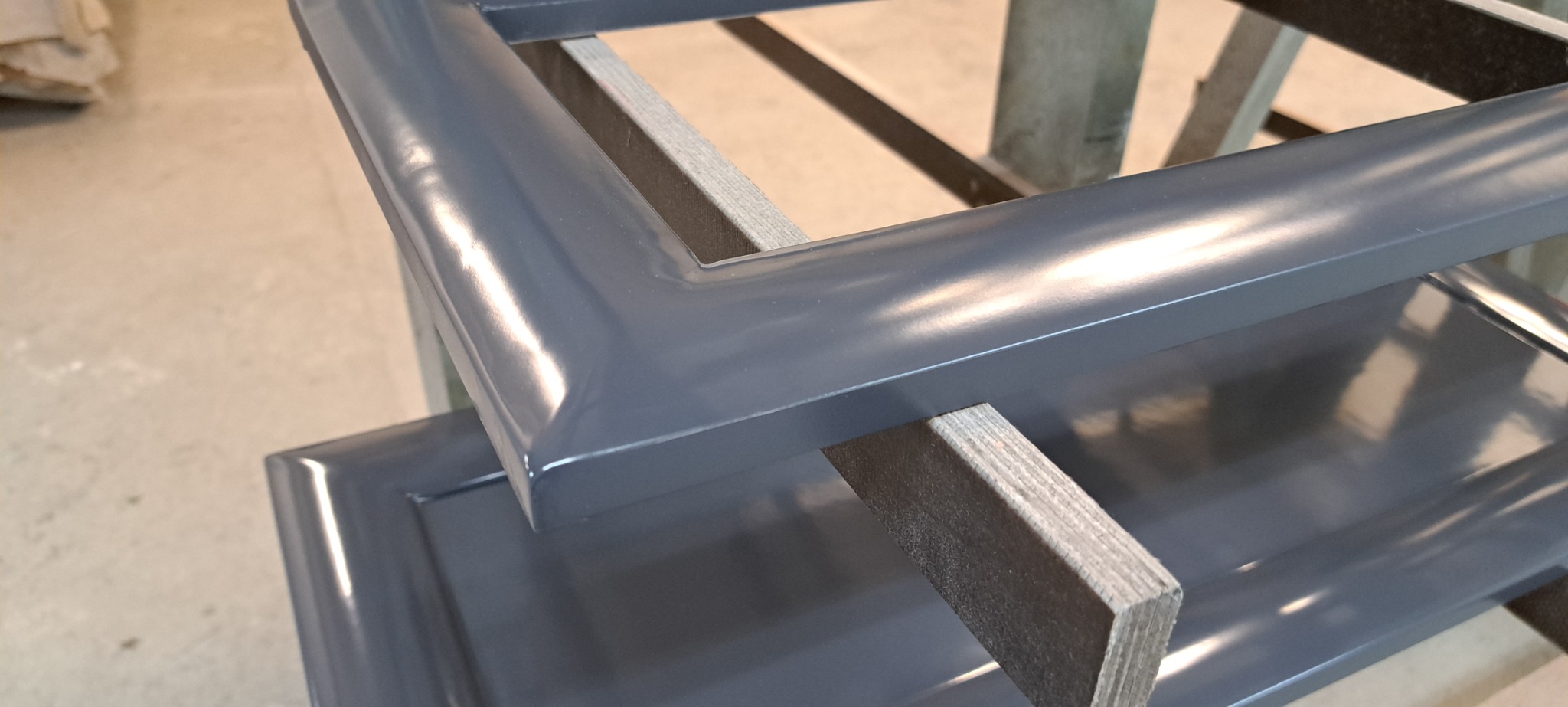 Szare, lakierowane fronty meblowe w trakcie schnięcia w warsztacie w Poznaniu, wsparte na drewnianych listwach.