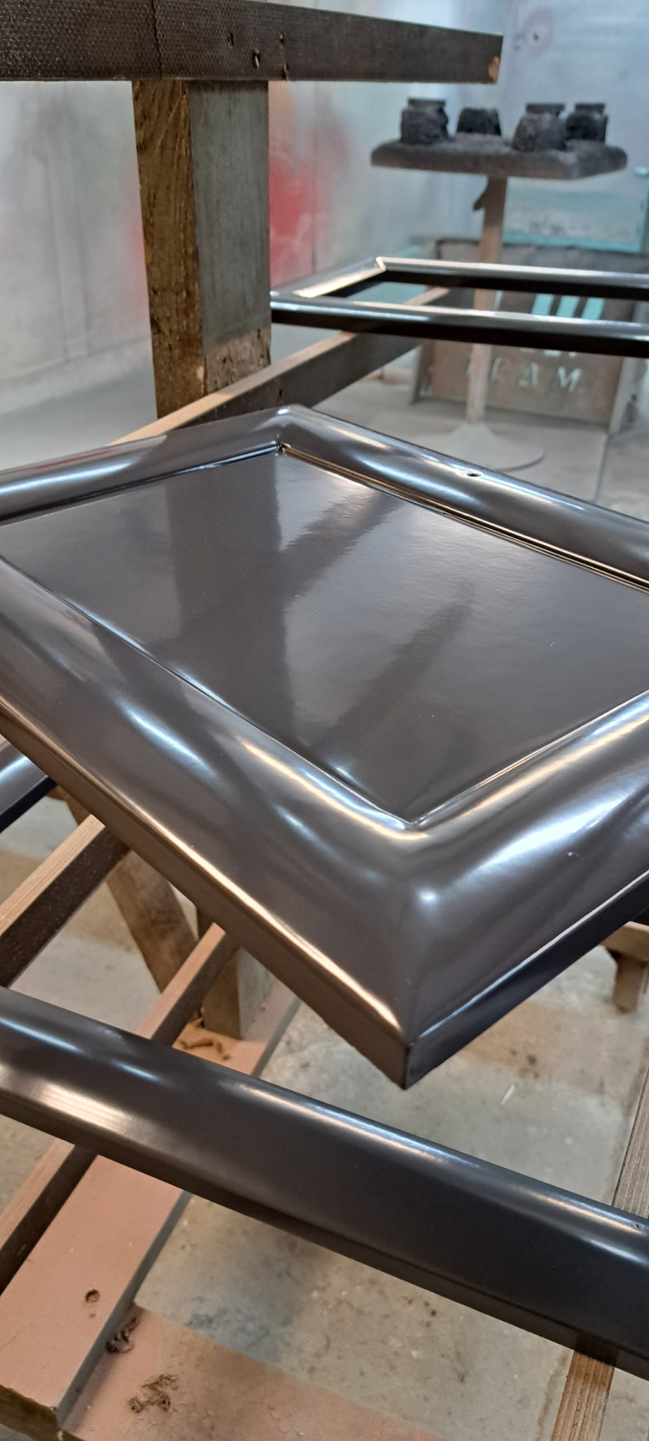 Lakierowane na szaro fronty meblowe podczas schnięcia na drewnianym stojaku w warsztacie.