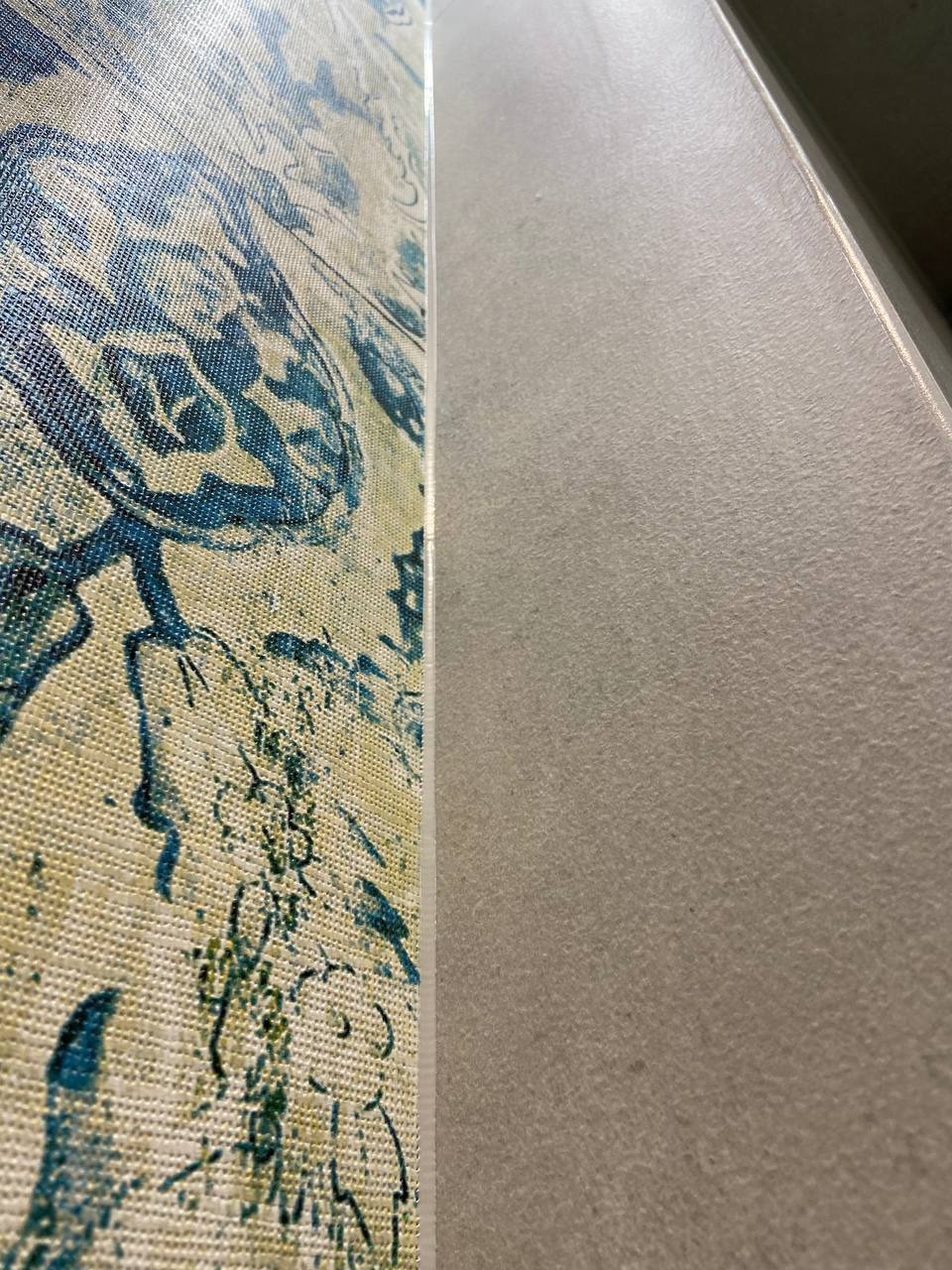 Fragment ściany z tapetą w niebiesko-żółte wzory i gładkiego, szarego panelu ściennego, widoczne z bliska pod kątem.