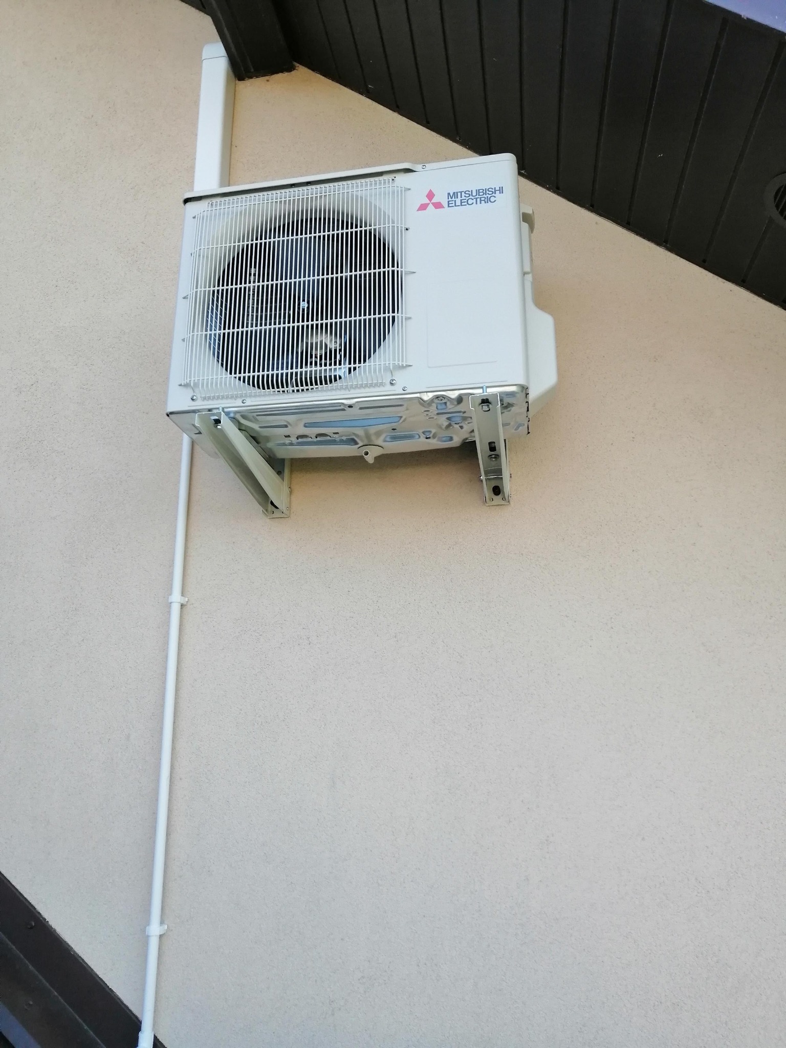 Zewnętrzna jednostka klimatyzacji Mitsubishi Electric zamontowana na jasnej ścianie budynku, widoczne rury odprowadzające skropliny.