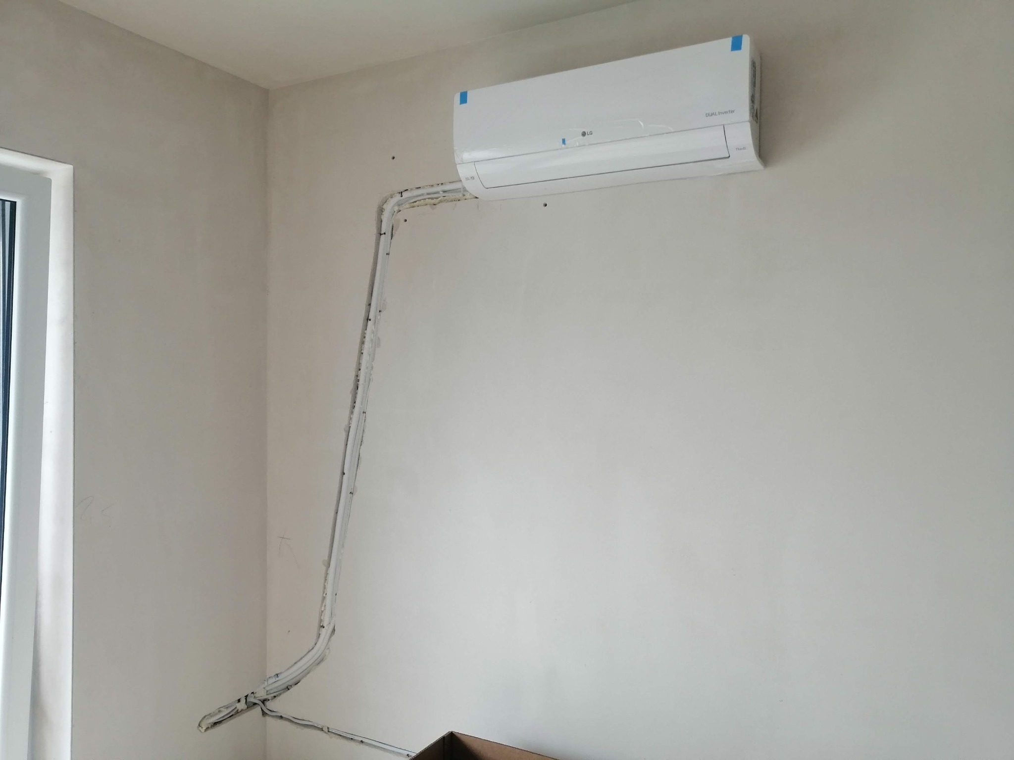 Świeżo zamontowany klimatyzator LG Dual Inverter na surowej ścianie, widoczne kable i rury prowadzone po powierzchni ściany przed ostatecznym wykończeniem.