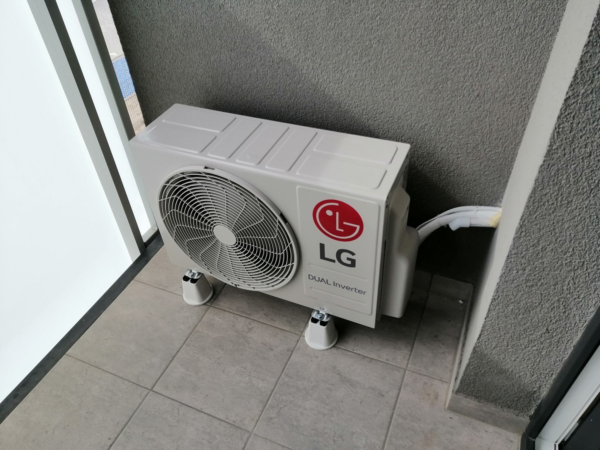 Jednostka zewnętrzna klimatyzacji LG Dual Inverter zamontowana na balkonie w Kole, widoczne przewody i wsporniki.