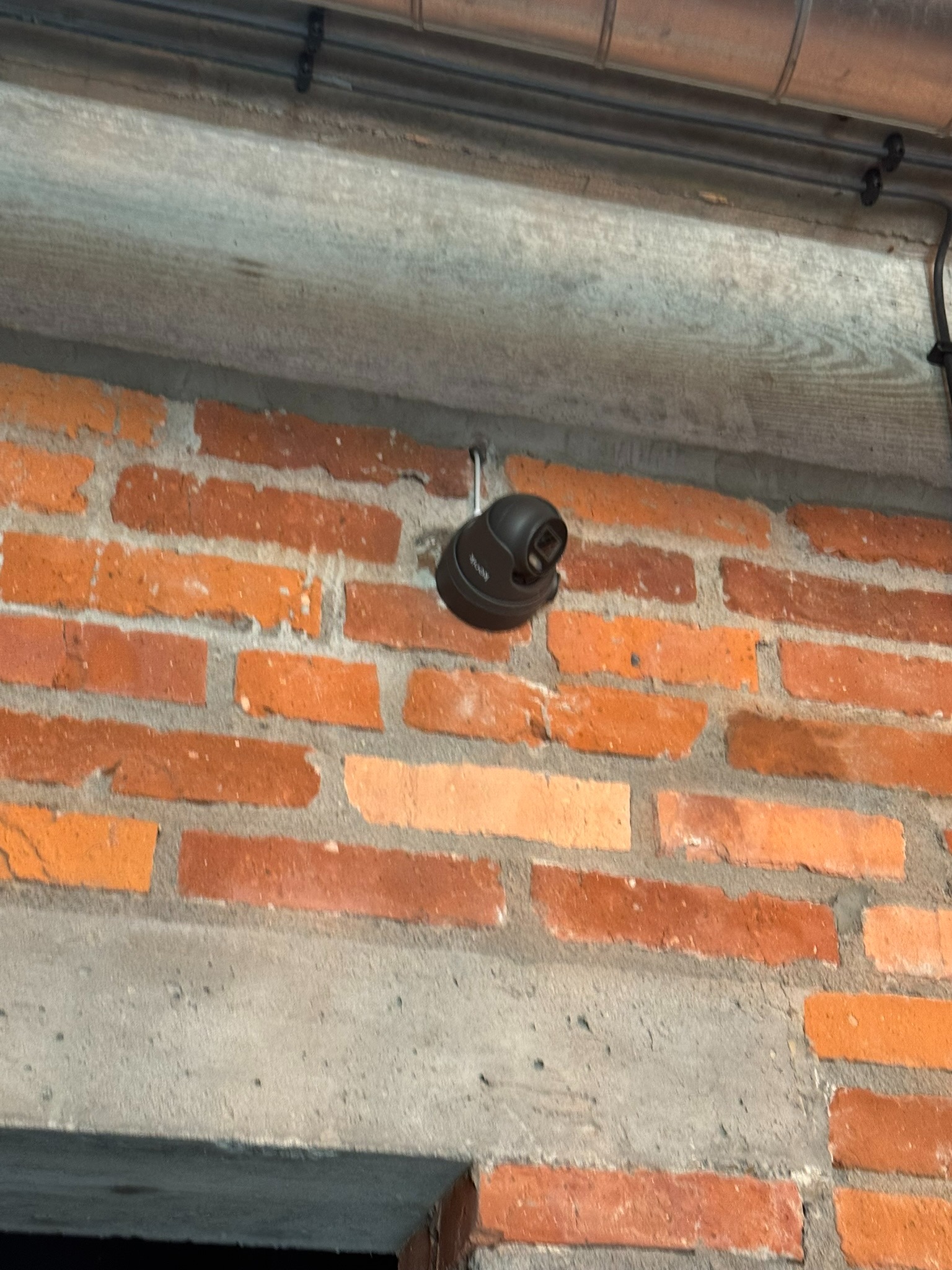 Kamera kopułkowa zamontowana na ceglanej ścianie z widocznymi przewodami i betonowym nadprożem.