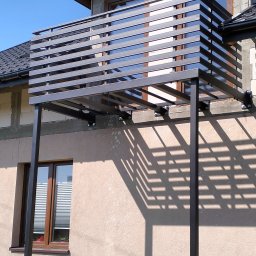 Łukasz Wolszczak - Nowoczesna, metalowa balustrada balkonowa z poziomymi szczeblami, zamontowana na elewacji budynku. Widoczne mocowania i cień konstrukcji.