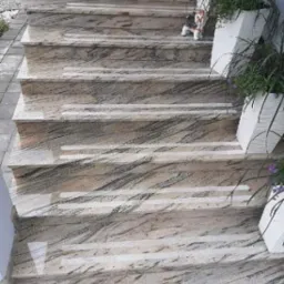 Zewnętrzne schody z kamienia o wzorze żyłkowym, zabezpieczone antypoślizgowymi paskami, z dekoracyjnymi donicami po bokach i figurką psa na jednym ze stopni.