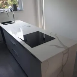 Jasny blat kamienny z wyraźnym wzorem żyłkowania, wbudowana płyta indukcyjna i zlew w nowoczesnej kuchni.