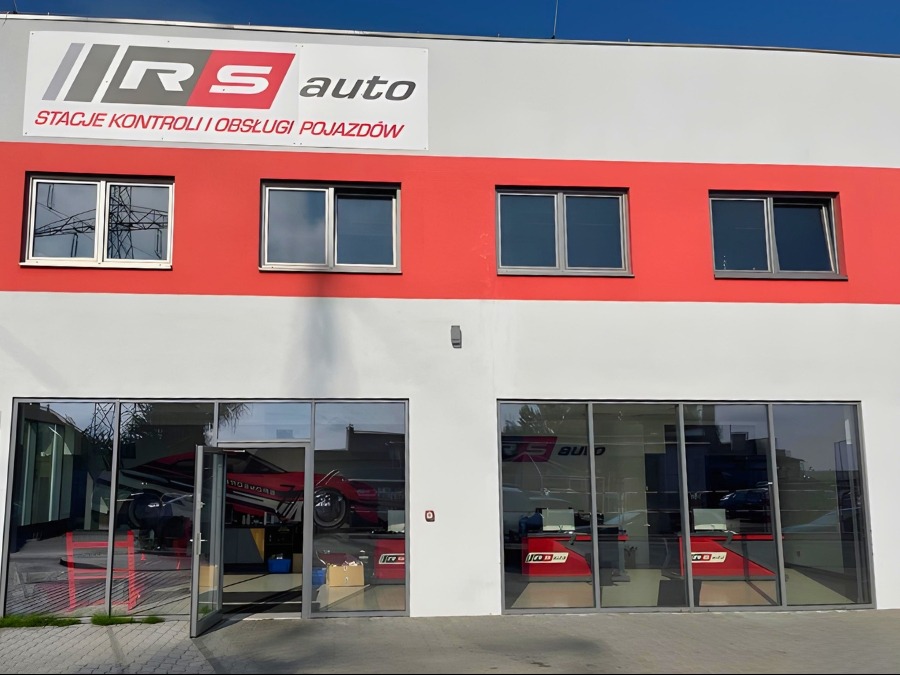 Fasada budynku warsztatu samochodowego RS Auto w Gdańsku z otwartymi drzwiami i widocznym wnętrzem, w którym znajduje się podnośnik samochodowy z czerwonym autem.