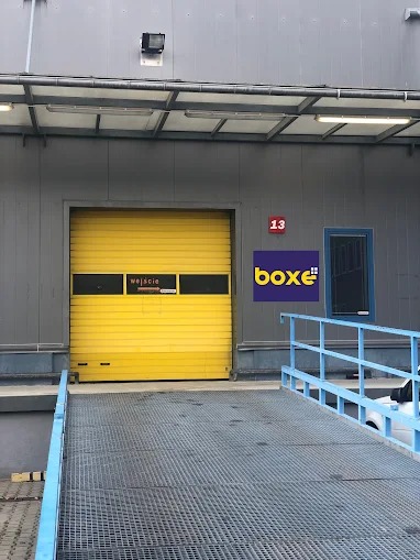 Żółta brama wjazdowa do magazynu z rampą, numerem 13 i logo firmy Boxe.