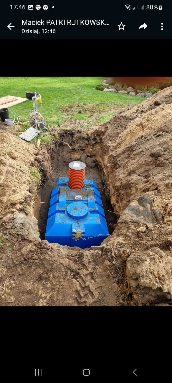 Niebieski, plastikowy zbiornik na szambo umieszczony w wykopie ziemnym, z widocznym kominkiem wentylacyjnym i śladami opon ciężkiego sprzętu na ziemi.