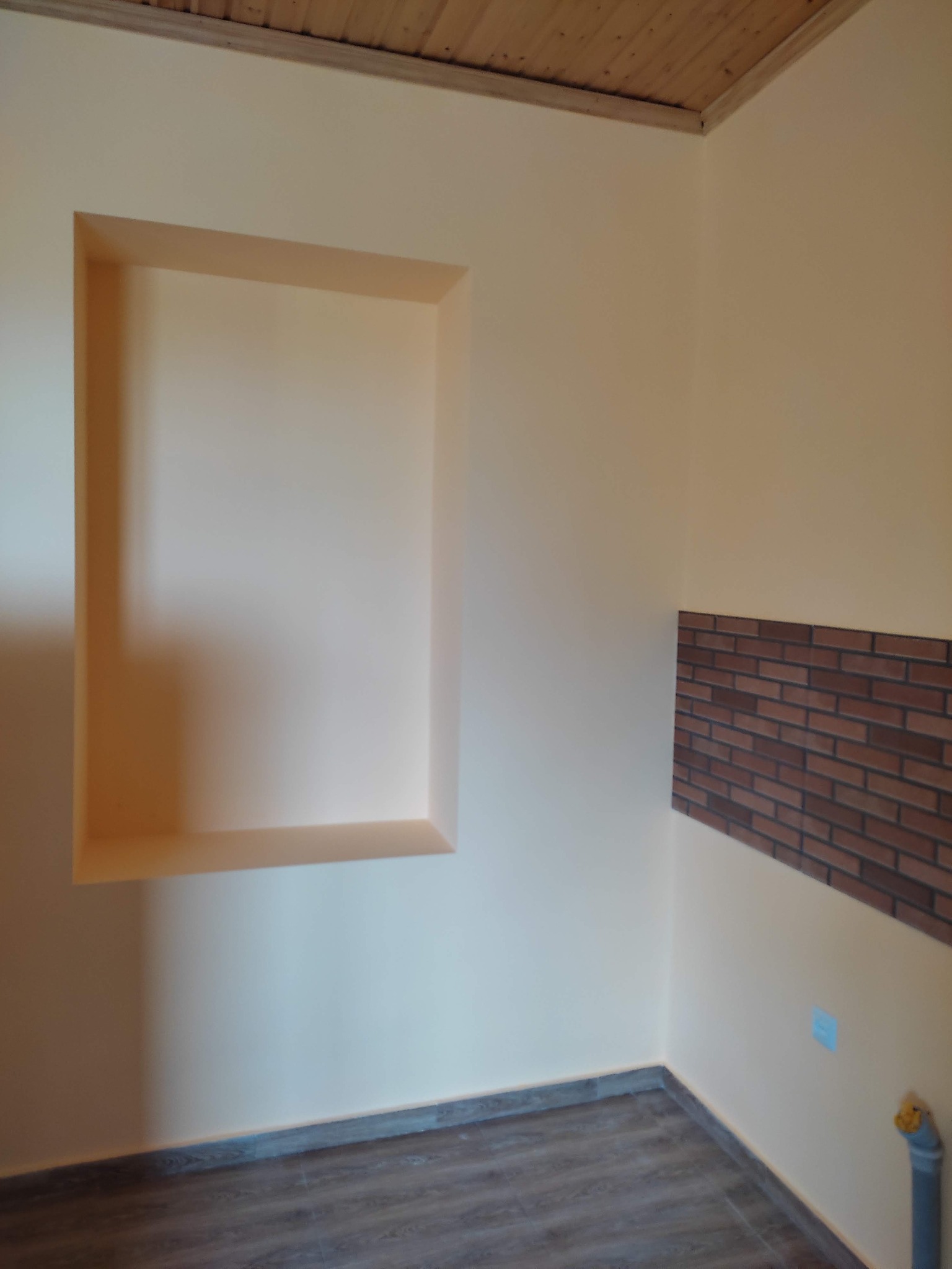 Wnęka w ścianie pomalowanej na kremowo, z fragmentem ściany wyłożonym cegiełkami i panelami podłogowymi w Bydgoszczy.