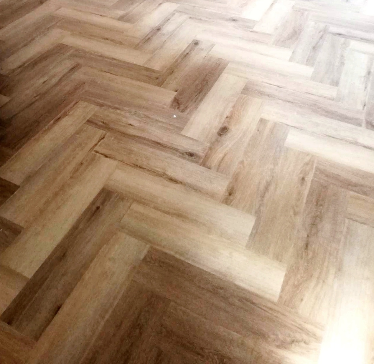 Jasne panele podłogowe ułożone we wzór jodełki francuskiej, z widoczną strukturą drewna i subtelnymi przebarwieniami.