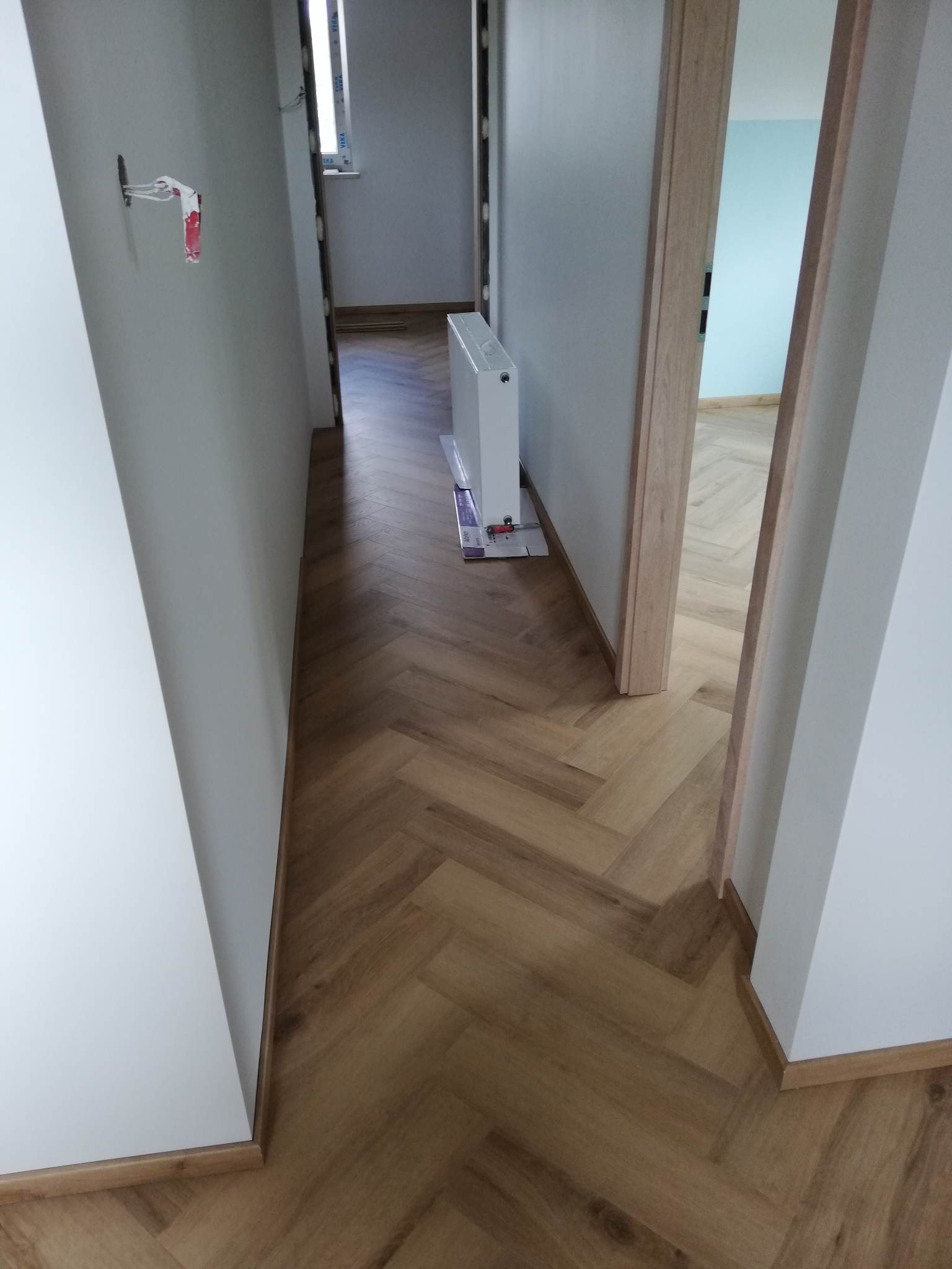 Korytarz po renowacji z nową podłogą z paneli ułożonych w jodełkę, świeżo pomalowane ściany i zamontowane drzwi.