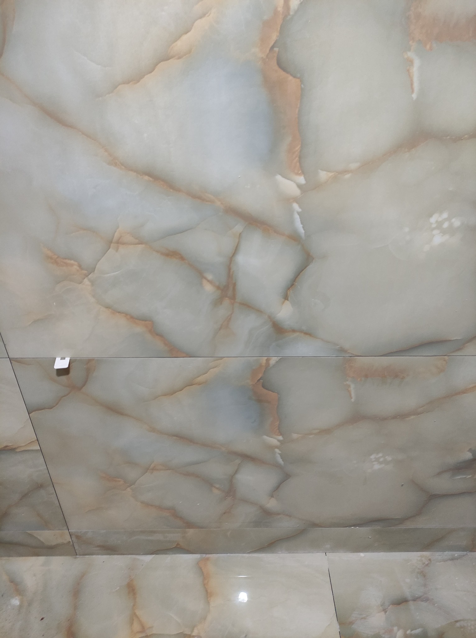 Ułożone płytki podłogowe o wzorze imitującym marmur w odcieniach beżu i brązu, z widocznym klipsem poziomującym spoinę.