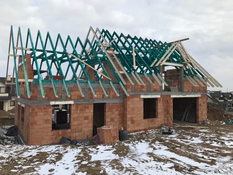 Budowa domu jednorodzinnego w Sierakowicach, widoczna konstrukcja dachu z zielonymi elementami i surowa cegła na ścianach, częściowo pokryta śniegiem.