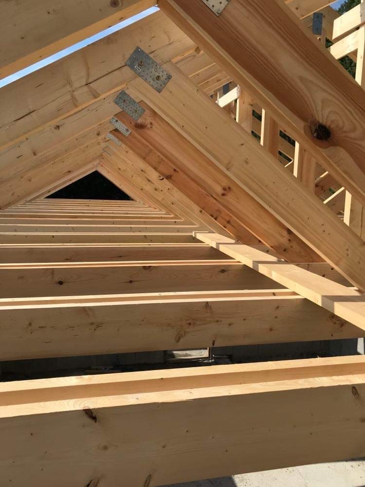 Drewniana konstrukcja więźby dachowej z widocznymi metalowymi łącznikami, jasne drewno, widok od wewnątrz, fragment nieba w tle.