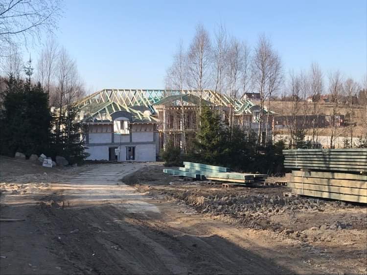 Konstrukcja drewniana dachu w trakcie budowy domu jednorodzinnego, widok z ziemi na budynek w stanie surowym otwartym, z przygotowanym materiałem budowlanym na pierwszym planie.