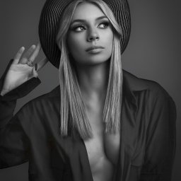 Archon studio fotograficzne Koszalin - Monochromatyczny portret kobiety w kapeluszu z paskami, z ręką uniesioną do twarzy, ubrana w rozpiętą koszulę, z długimi blond włosami i wyrazistym makijażem.
