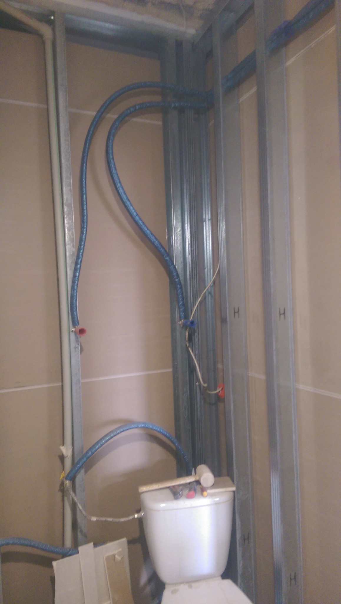 Instalacja wodna i elektryczna w łazience w Gliwicach, widoczne rury w oplocie, metalowa konstrukcja ścianki działowej i częściowo zamontowana toaleta.