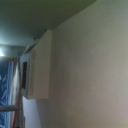 KamBud - Ściana po szpachlowaniu, widoczny narożnik i fragment sufitu, w tle drabina malarska i zakryte folią drzwi.