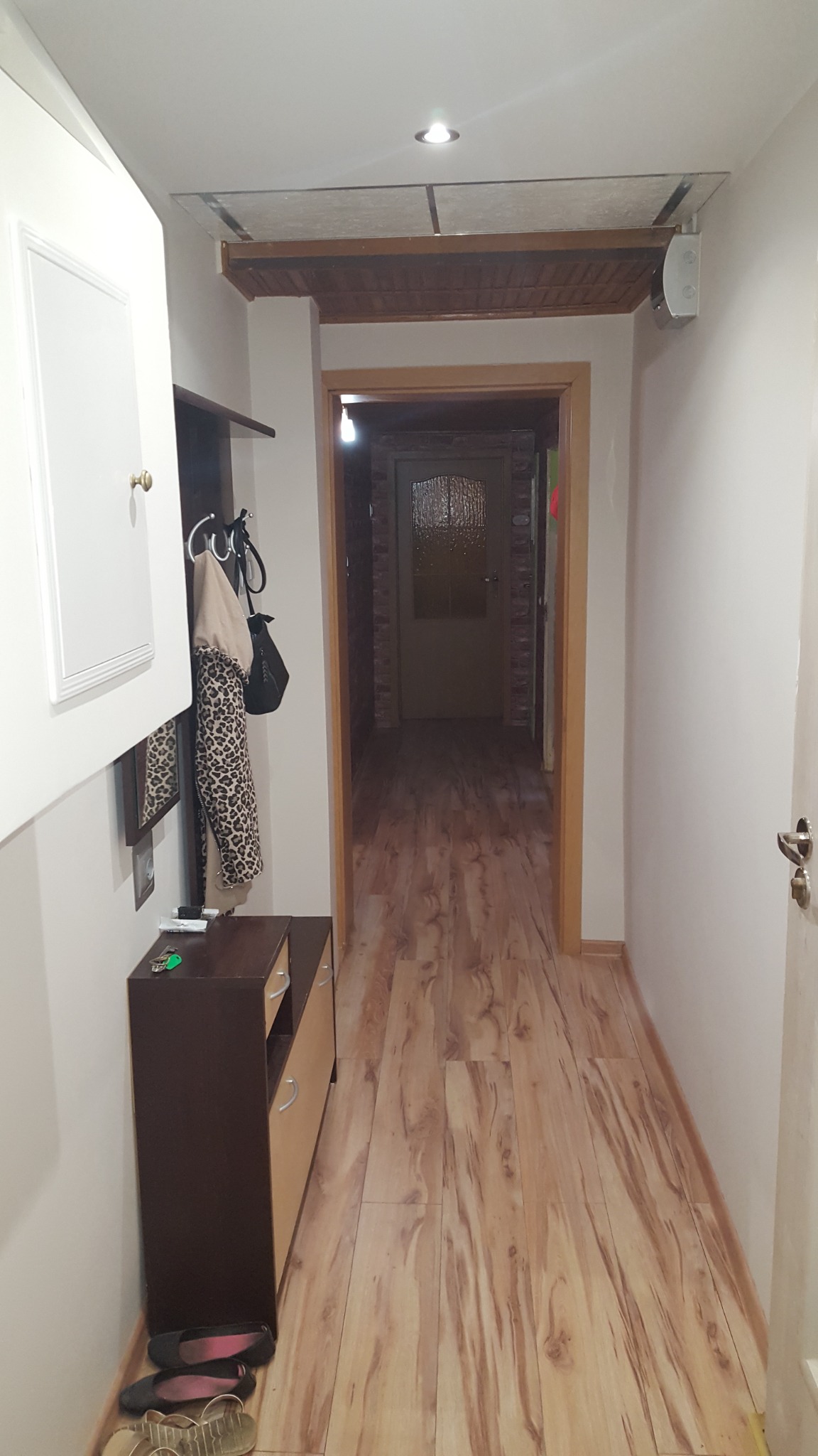 Korytarz po remoncie z drewnopodobną podłogą, szafką z wieszakiem, widokiem na dalsze pomieszczenia i podwieszanym sufitem z oświetleniem punktowym.