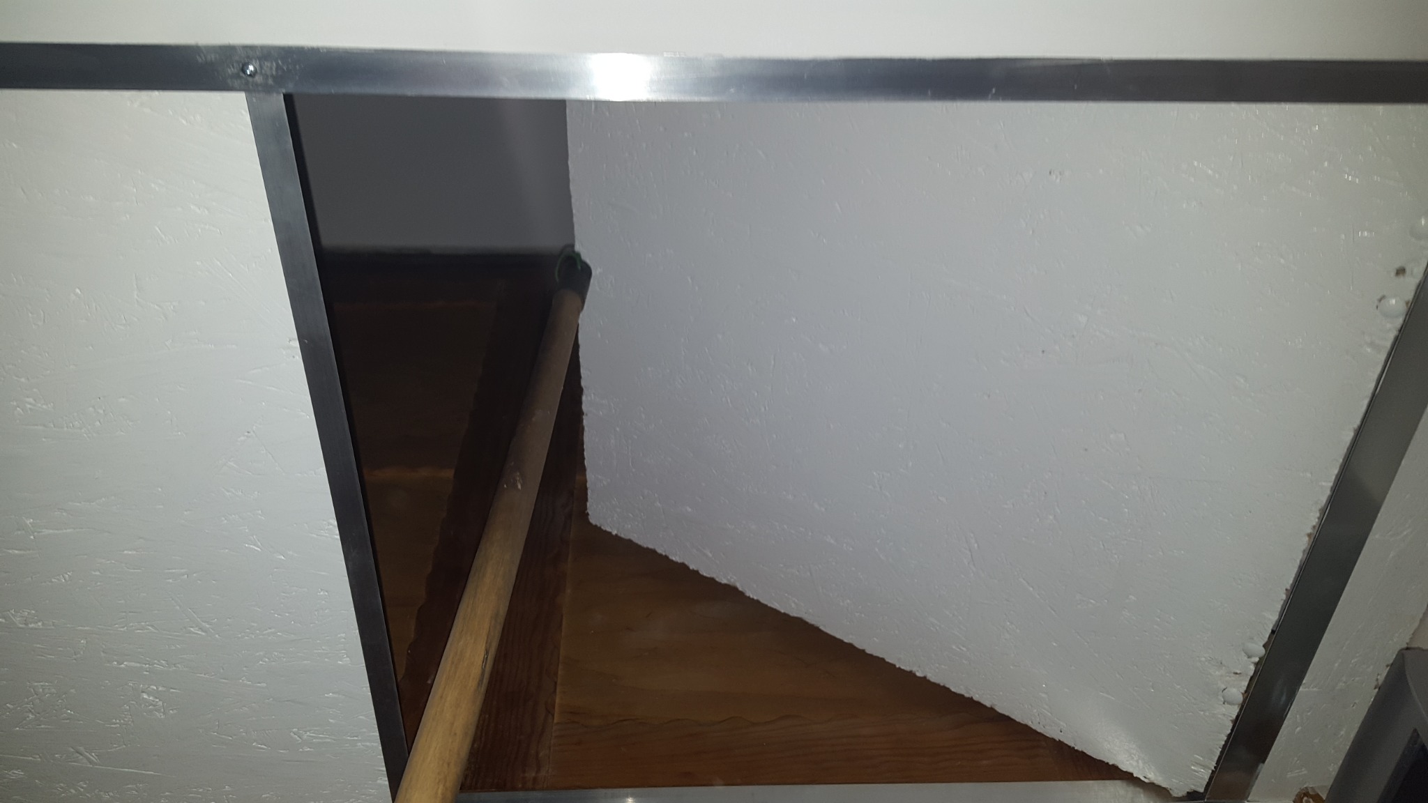 Malowana białą farbą ściana poddasza z widoczną drewnianą konstrukcją i fragmentem wałka malarskiego z zieloną rączką.