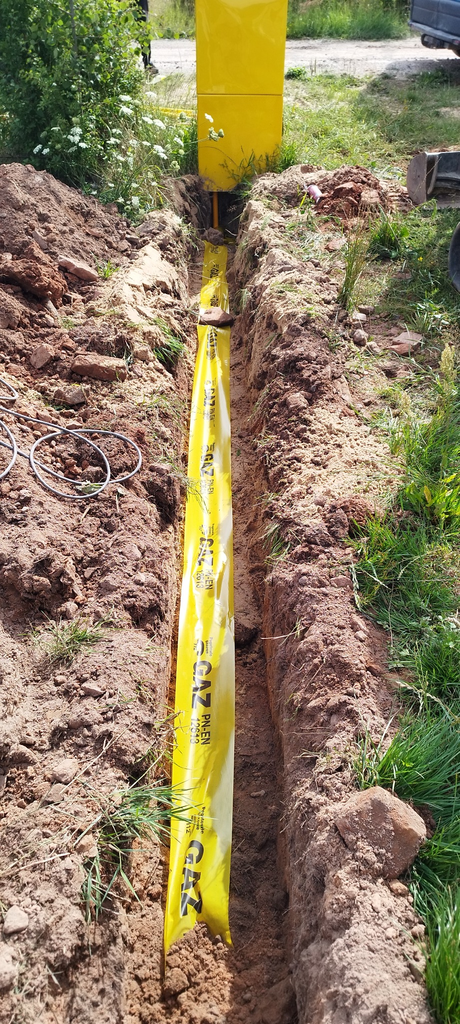 Wykopany rów z żółtą folią ostrzegawczą GAZ PN-EN, widoczna instalacja gazowa i żółta szafka gazowa na powierzchni.
