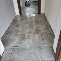 Korytarz z szarymi płytkami imitującymi kamień, widok w głąb mieszkania, zarys drzwi po bokach.