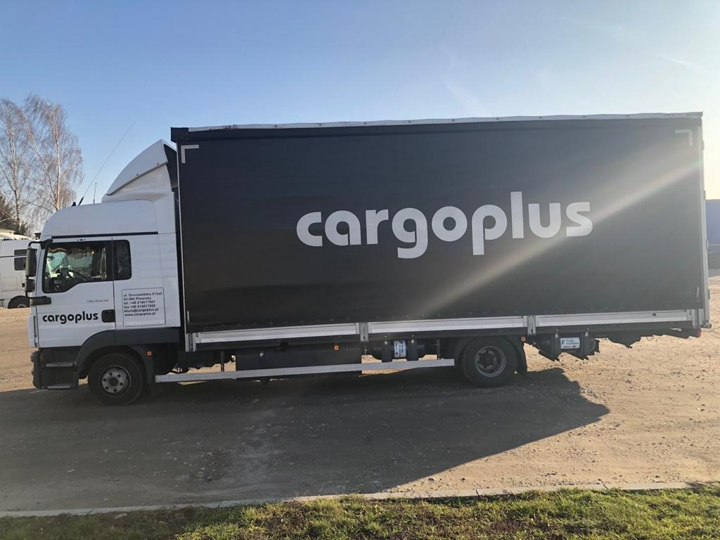 Ciężarówka CargoPlus z czarną plandeką na tle błękitnego nieba, widok z boku, oświetlona słońcem.