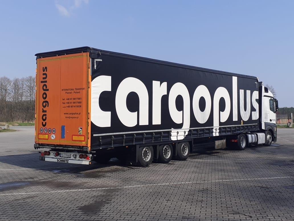 Ciężarówka z naczepą firmy Cargoplus, widoczna z boku, zaparkowana na placu z kostki brukowej, z pomarańczowo-czarną grafiką na naczepie i numerami kontaktowymi.