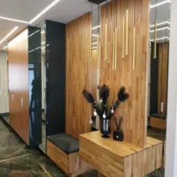 Nowoczesny przedpokój z zabudową szaf, drewnianą boazerią, lustrami, wiszącymi lampami i marmurową podłogą z złotymi żyłami.